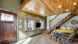 A spacious living area with a wooden ceiling, a staircase, a sofa, and a television.