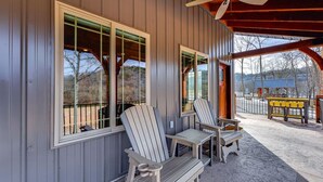 A covered porch with Adirondack chairs, a ceiling fan, and a view of the surrounding landscape.