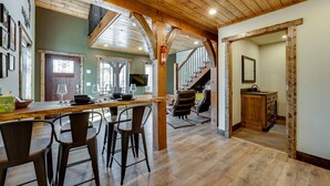 A spacious kitchen with a wooden ceiling, a dining area with bar stools, and a staircase leading to an upper level.