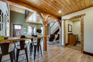 Une cuisine spacieuse avec un plafond en bois, un coin repas doté de tabourets de bar et un escalier menant à un niveau supérieur.
