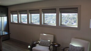 Una habitación con cocina, una zona de estar con dos sillas y un ventanal con vistas a árboles.