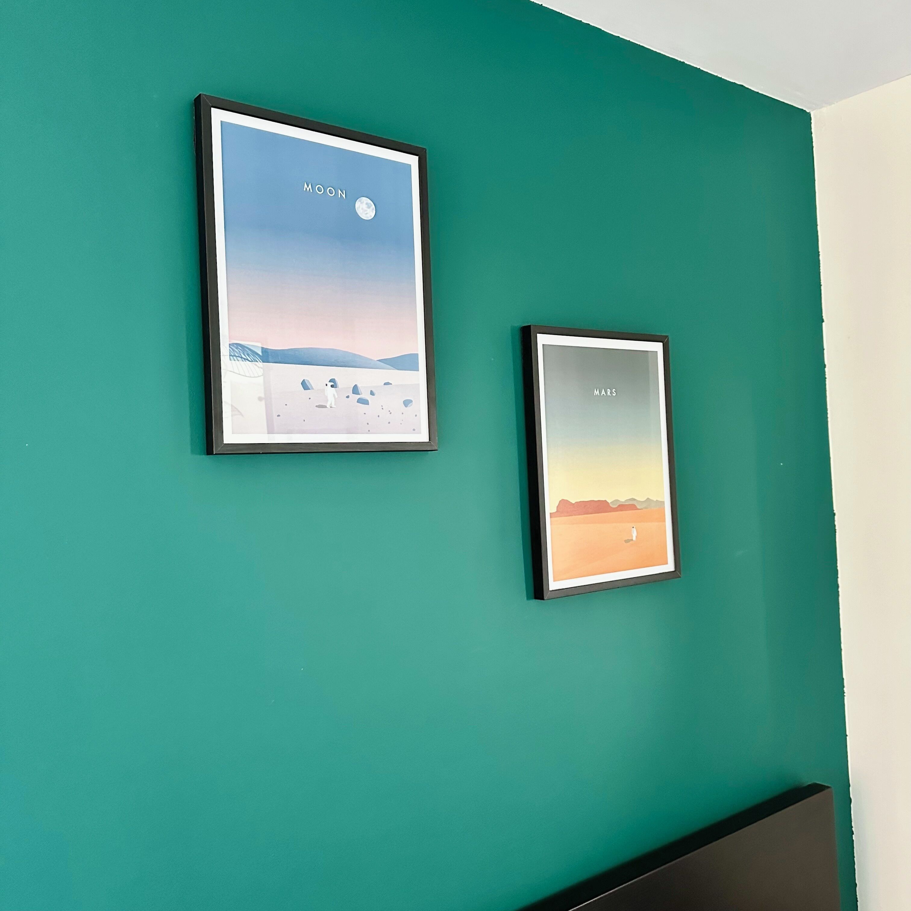 Deux œuvres d’art encadrées ornent un mur de couleur turquoise : l’une représente la lune, l’autre, la planète Mars.