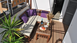 A balcony with a sofa, cushions, a table with a bottle and glasses, and potted plants.