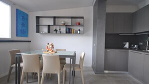 A modern kitchen with grey cabinets, a built-in oven, and a dining area with a glass table and chairs.