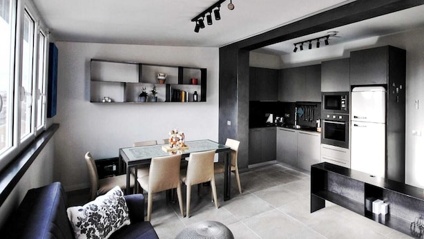 A modern kitchen with built-in appliances, a dining area with a glass table, and a living room with a sofa and a decorative pillow.
