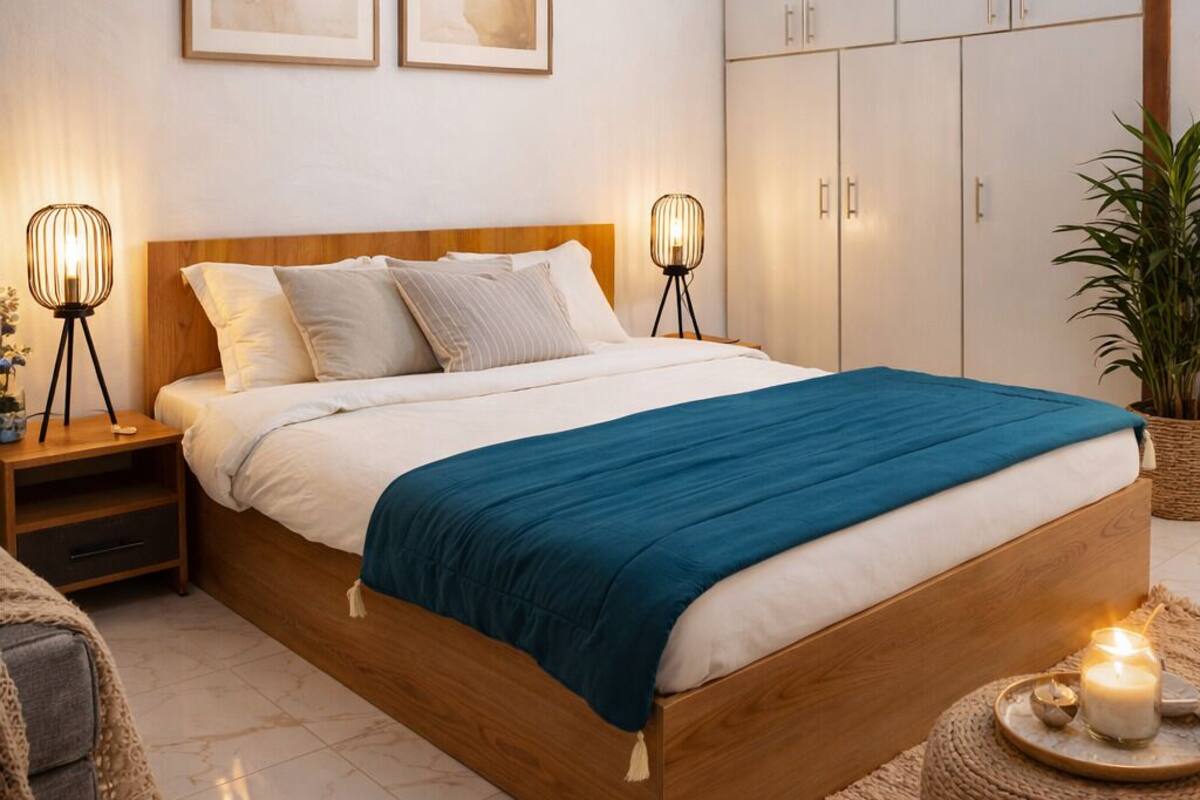 A bedroom with a wooden bed, two bedside lamps, a blue bedspread, a large wardrobe, and two abstract paintings on the wall.
