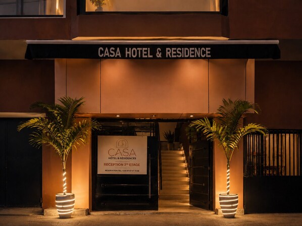 The entrance to Casa Hotel & Residence with a reception desk, two potted plants, and a staircase leading to the entrance. - Casa Hôtel Résidence (Abidjan)
