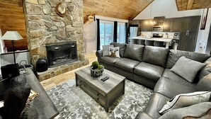 Una sala de estar acogedora con chimenea de piedra, sofá de cuero y una mesa de centro.