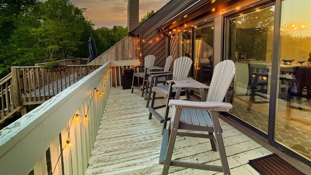 Una terraza con sillas y mesas, barandilla de madera y pared de vidrio.