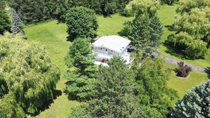 A large house surrounded by dense trees and a well-maintained lawn.
