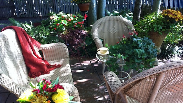 Un'area patio con sedie in vimini, un tavolo con un vaso di fiori e piante in vaso.