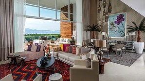 A spacious living area with a large window, a sofa set, a coffee table, and a dining area with chairs and a table.