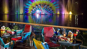 A nighttime view of a waterfront restaurant with colorful fountains and outdoor seating.