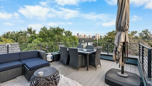Eine Dachterrasse mit Gartenmöbeln, darunter eine Sitzecke mit Sofa, Esstisch und Stühlen, sowie ein Sonnenschirm.