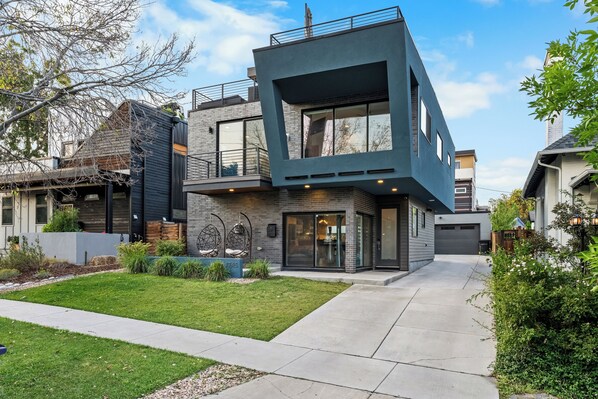 A modern two-story house with a flat roof, large windows, and a well-maintained lawn.