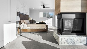 Ein modernes Schlafzimmer mit Bett, Deckenventilator, Kamin und großem Fenster.