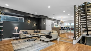 Ein modernes Wohnzimmer mit einer Couch, einem Couchtisch und einem Teppich. Eine Treppe mit Geländer führt zu einer oberen Ebene.
