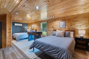 Quarto de cabana de madeira com duas camas, uma escrivaninha e uma janela.