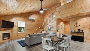 Ein Holzblockhaus-Interieur mit Essbereich, Sofa, Kamin und Treppe.