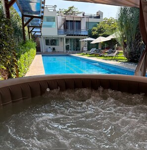 Un bain à remous avec vue sur une piscine et une maison moderne en arrière-plan.