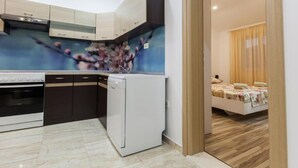 A modern kitchen with a built-in oven, a white refrigerator, and a microwave. There is a dining area with a table and chairs, and a wooden floor.