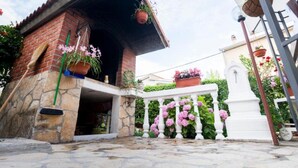 A stone building with a tiled roof, a white fence with pink flowers, and a white statue in the background.