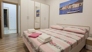 A bedroom with a bed, a wardrobe, a nightstand, and a painting of a coastal scene.