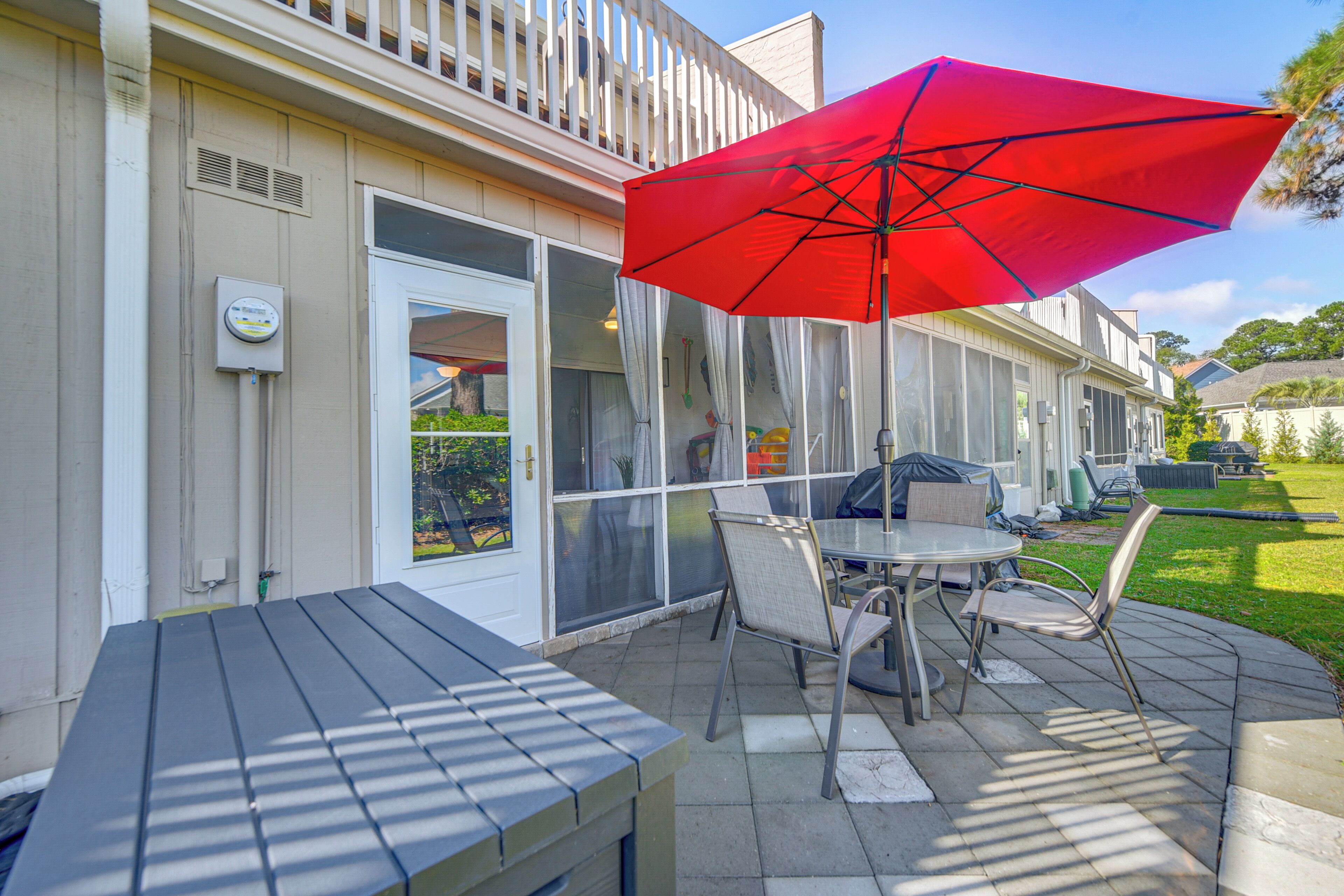 Une terrasse extérieure avec une table et des chaises, un parasol rouge et un espace salon abrité.