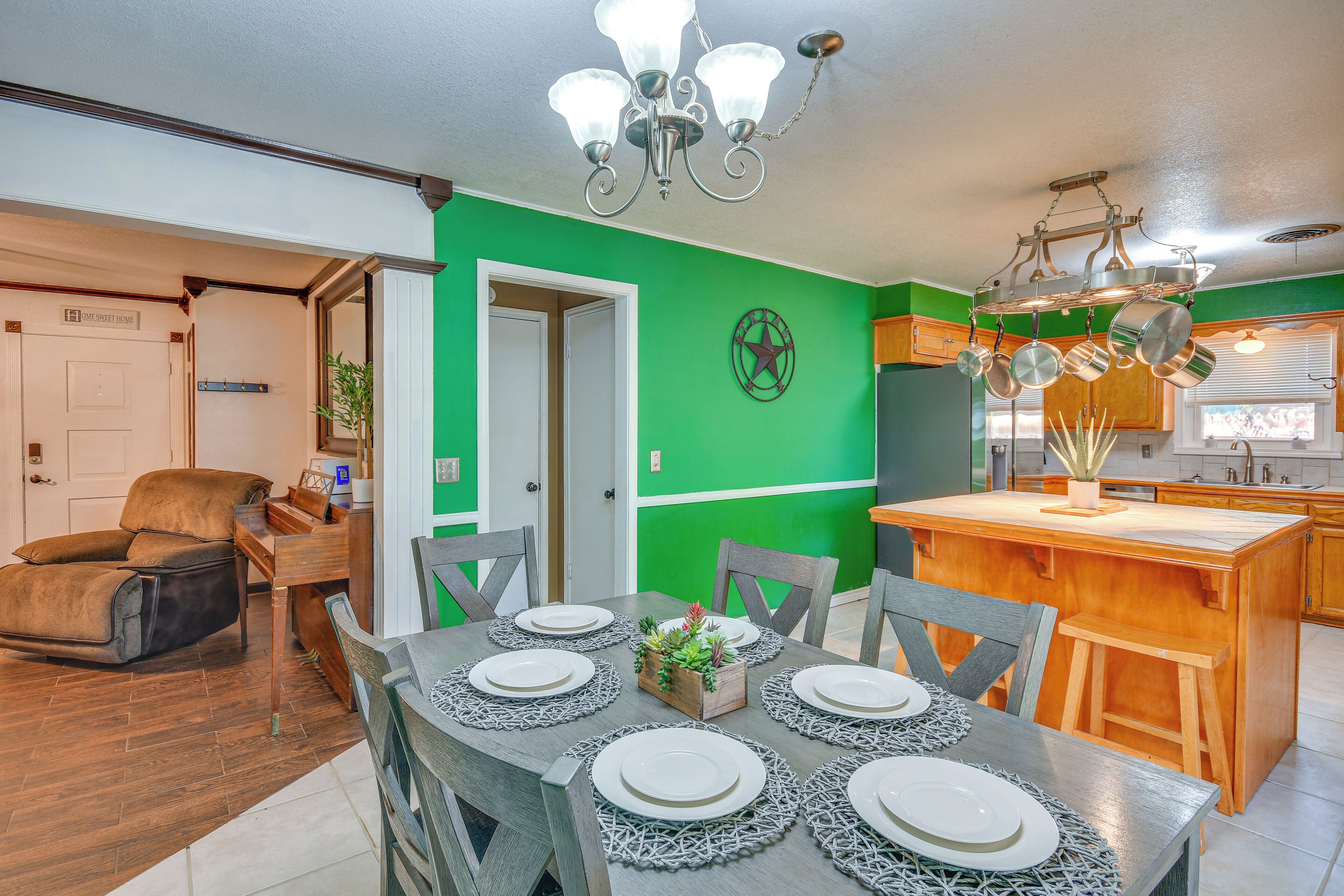 Un coin repas avec une table dressée pour six personnes, une cuisine avec des ustensiles de cuisine suspendus et un mur d’accent de couleur verte.