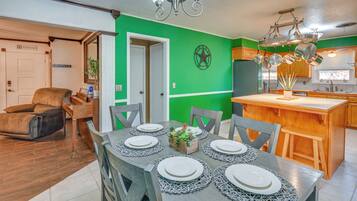 Un coin repas avec une table dressée pour six personnes, une cuisine avec des ustensiles de cuisine suspendus et un mur d’accent de couleur verte.