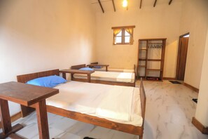A room with two wooden beds, a small table, a shelf, and a window with curtains. - Mango Tree Retreat (Galewela)