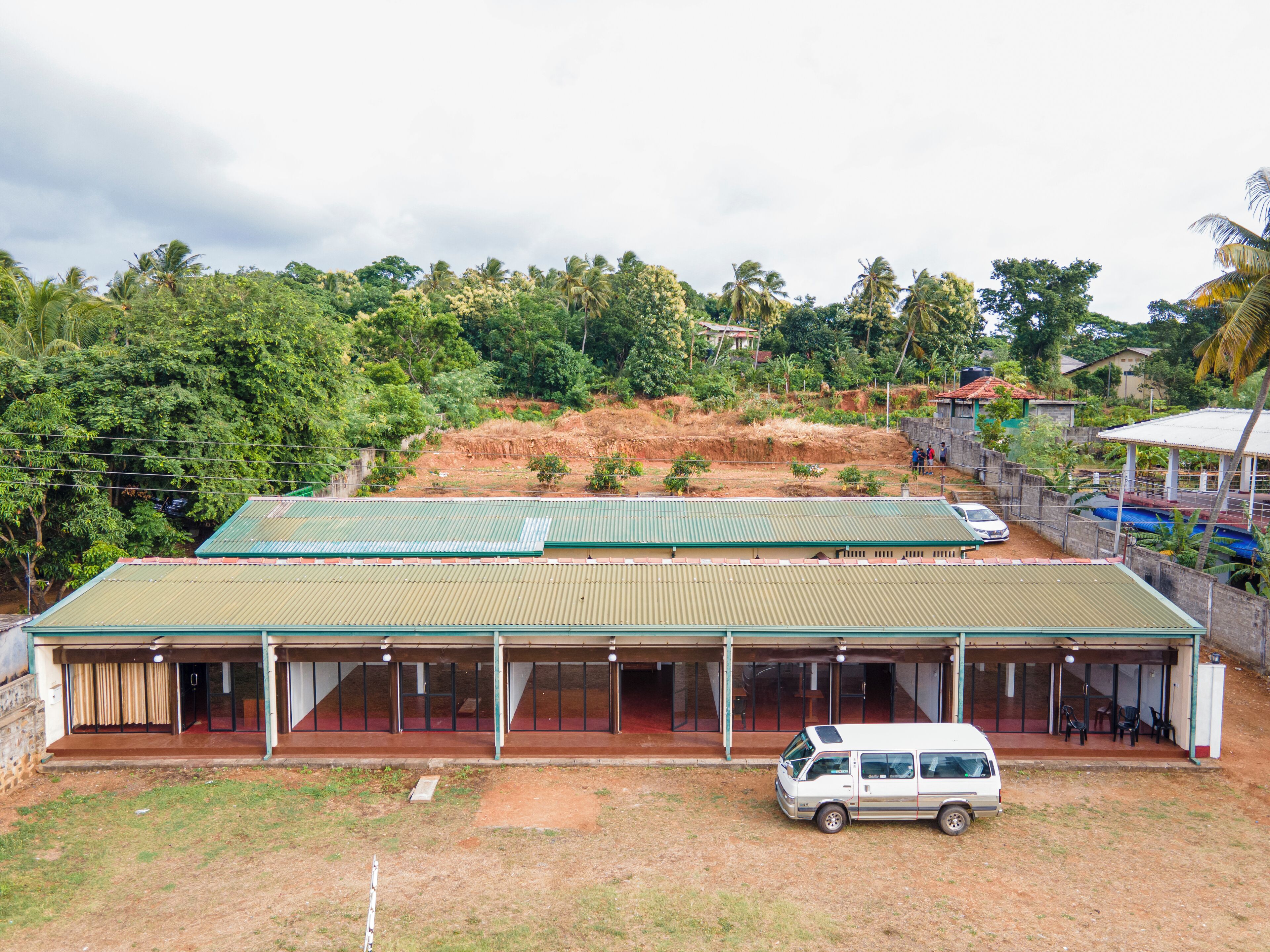 A building with a green roof, a white van parked in front, and a dirt area in front of the building.