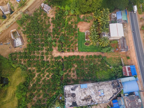 An aerial view of a rural area with scattered buildings, a dirt road, and dense vegetation. - Mango Tree Retreat (Galewela)