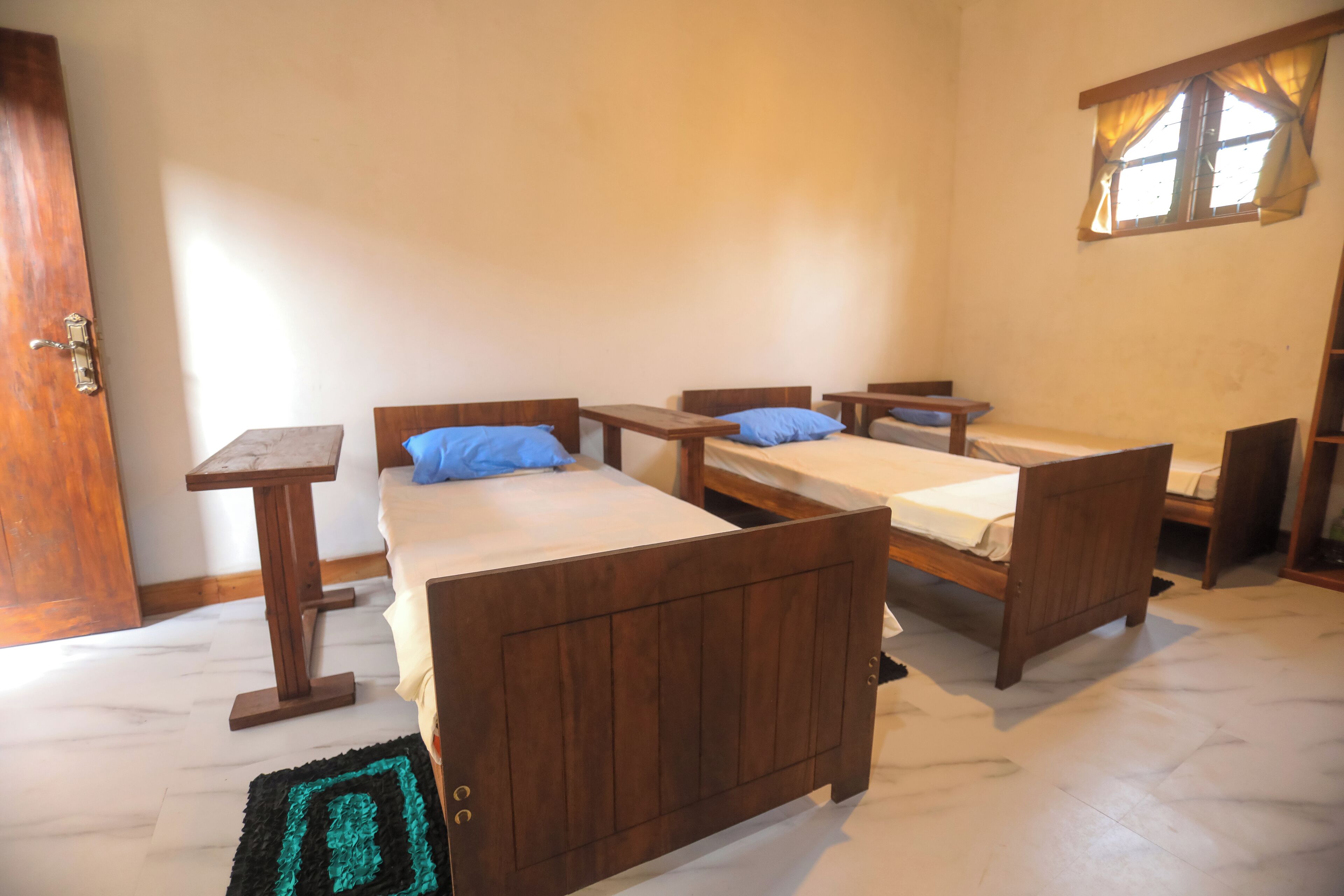A room with two wooden beds, a small table, and a window with curtains.