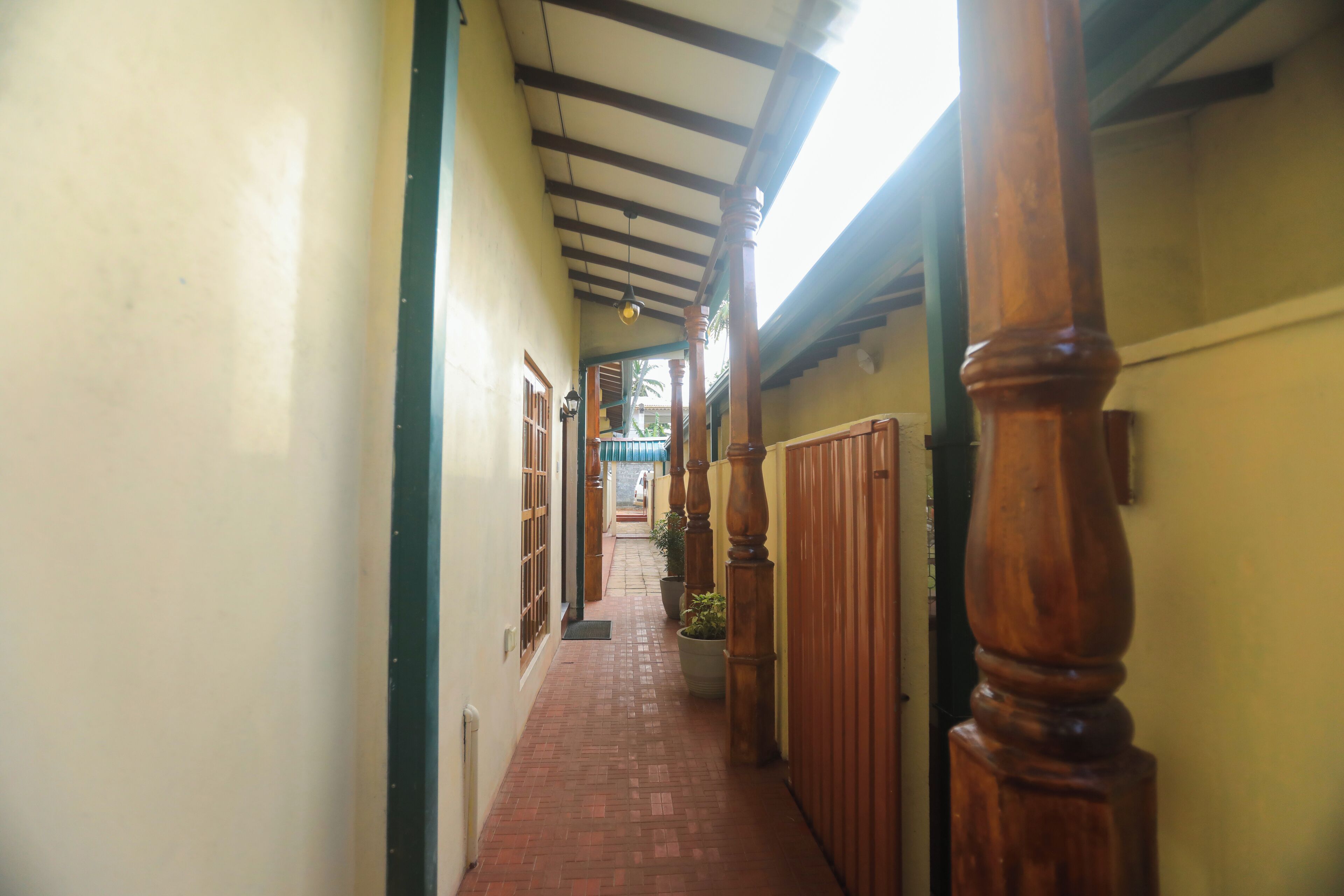 Um corredor estreito com piso de azulejos, colunas de madeira e teto com vigas aparentes.