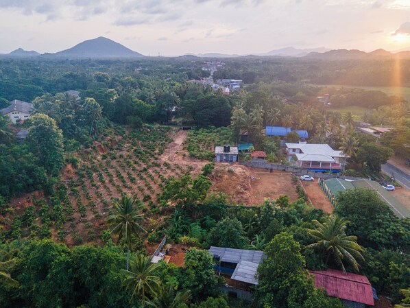 An aerial view of a rural area with scattered houses, a road, and a mountain in the background. - Mango Tree Retreat (Galewela)