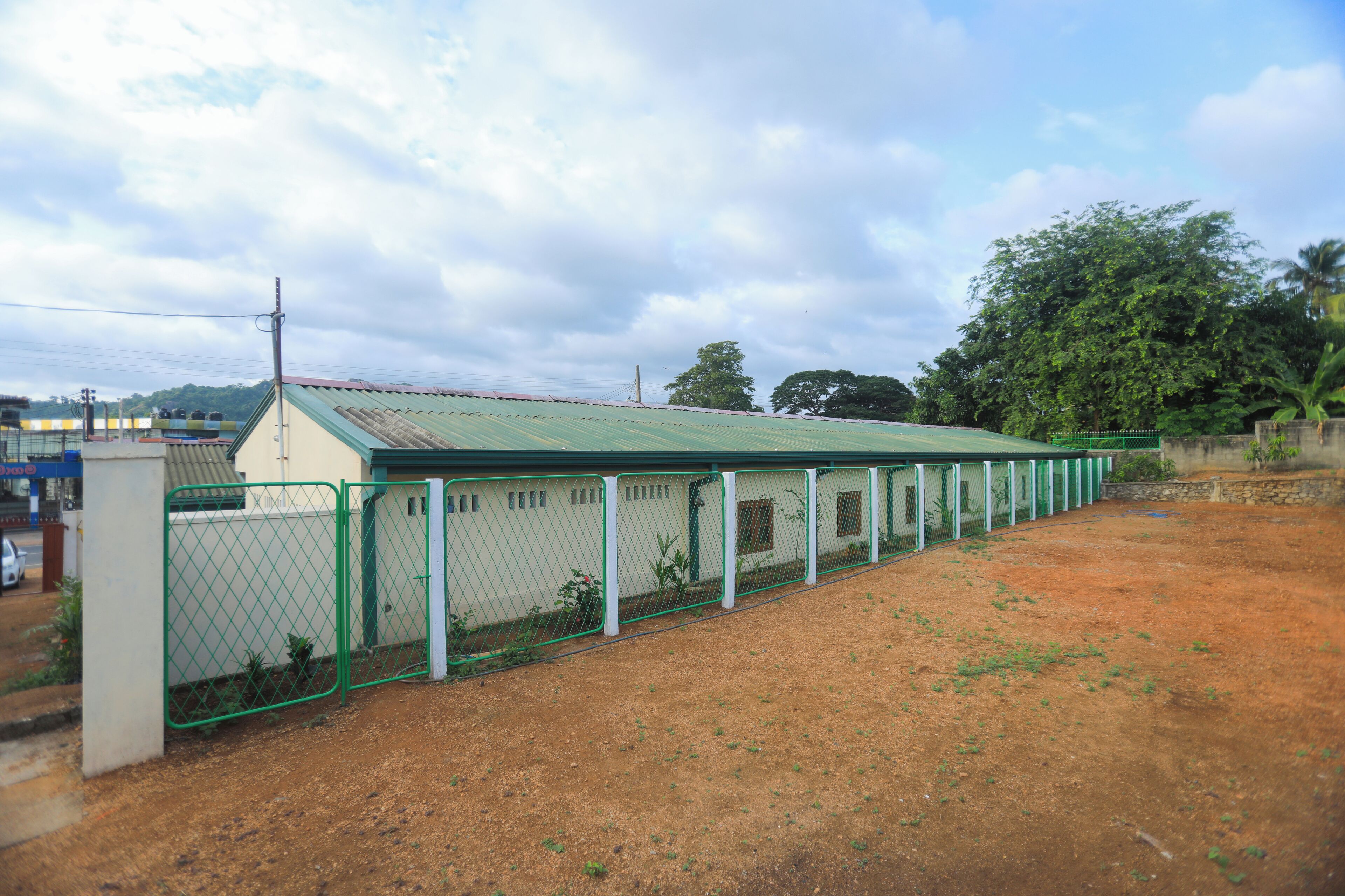 A fenced outdoor area with a building that has a green roof and a white wall.