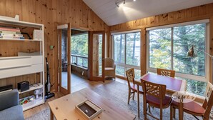 A wooden cabin interior with a dining area, bookshelves, and a view of the forest. - Darling 3 bed 2 bath cottage on Lake Joseph with Bunkie! NW Exposure! Boathouse (Seguin)