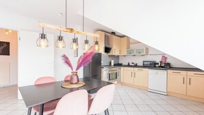 A modern kitchen with wooden cabinets, a black countertop, and a dining area with pink chairs and a black table.