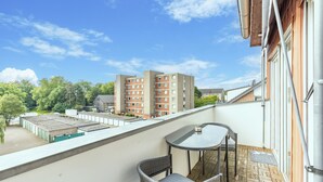 A balcony with a table and chairs, overlooking a parking area and buildings.