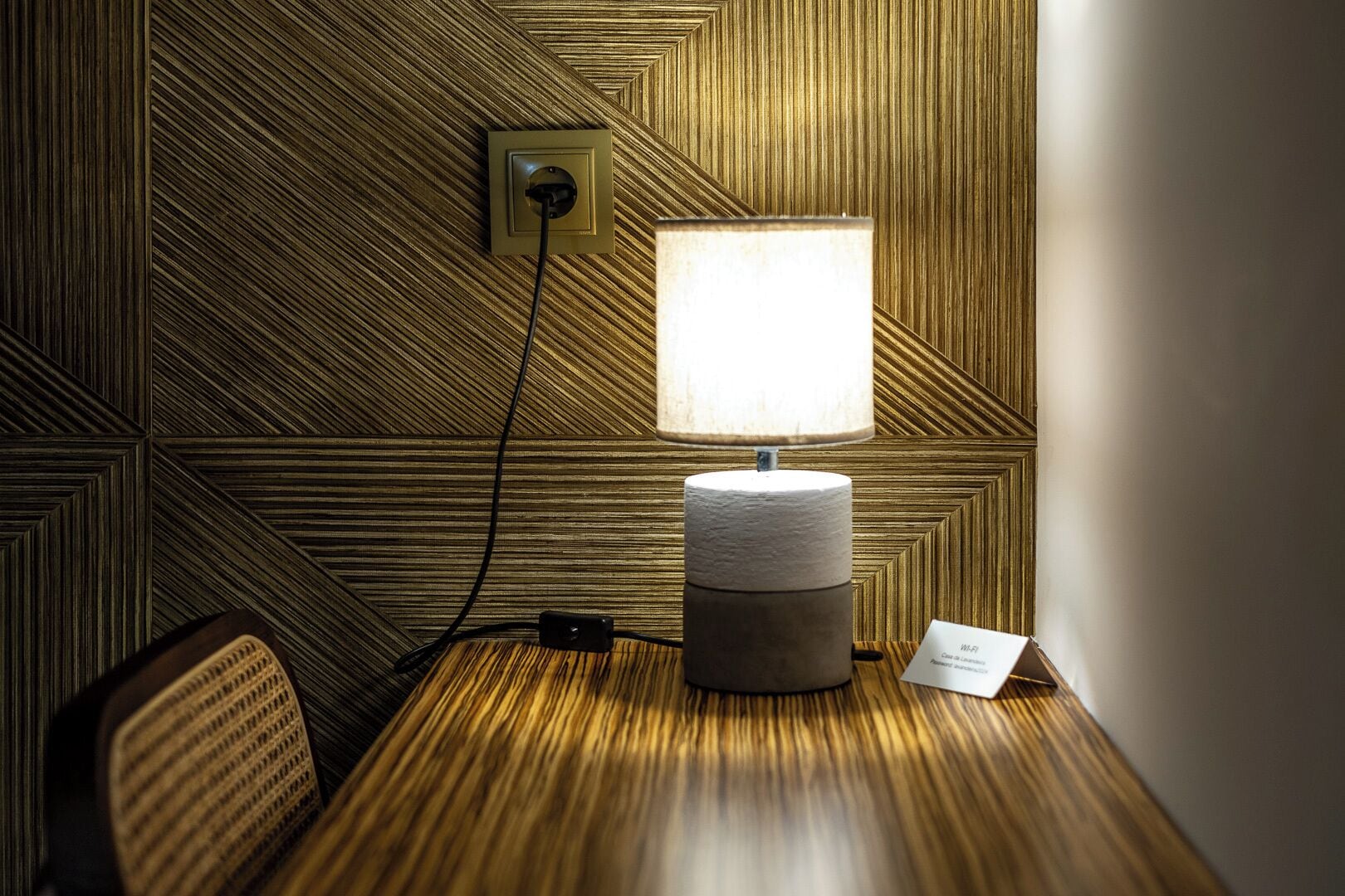 A room with a patterned wall, a lamp, a power outlet, and a sign indicating Wi-Fi availability.