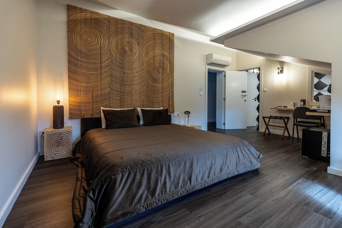 Un dormitorio moderno con una cama grande, una lámpara de noche, un cabecero de madera, un escritorio con silla y un equipo de aire acondicionado.