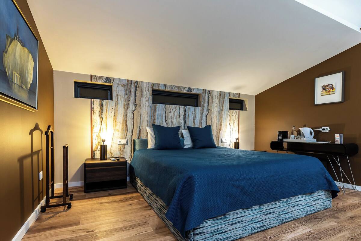 Un dormitorio con cama, mesitas de noche, un escritorio y un cuadro en la pared.