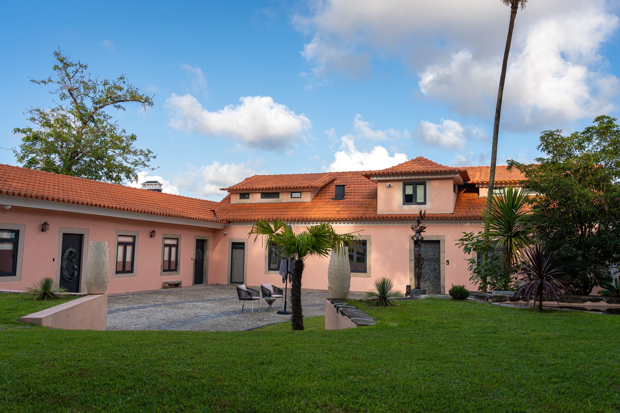 Edificio de dos plantas con techo de tejas, un patio con una palmera y un césped bien cuidado.