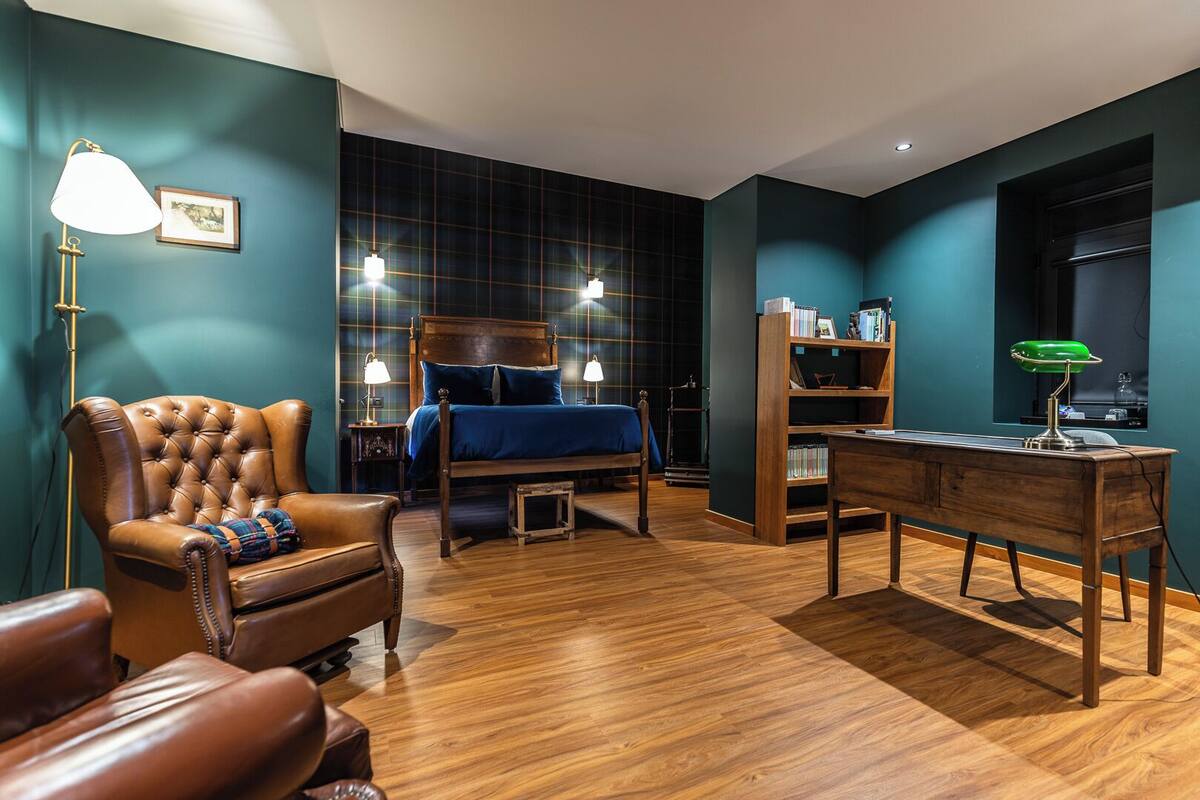 Un dormitorio con cama, un sillón de cuero, un escritorio de madera y una estantería.