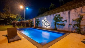 Ein Swimmingpool mit einer versunkenen Sitzgruppe und einer Wand mit beleuchteten architektonischen Elementen.