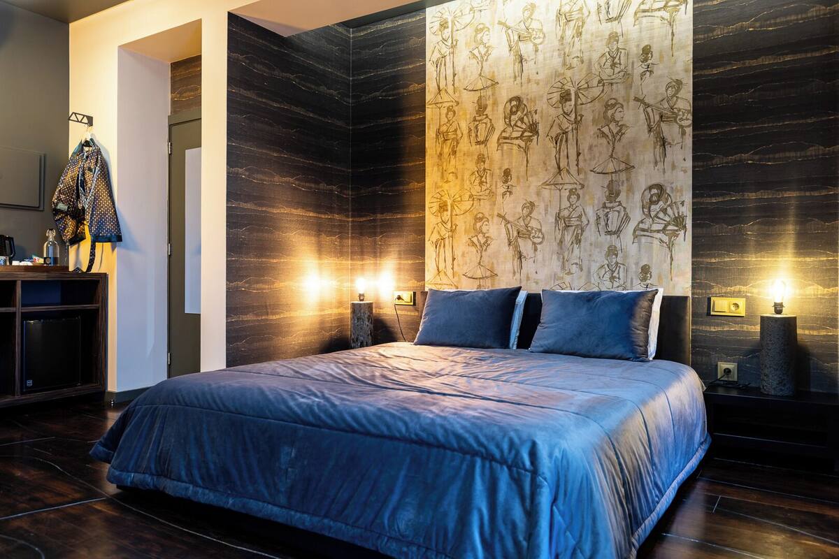 Un dormitorio moderno con una cama grande, suelo de madera oscura y una pared decorada con obras de arte tradicionales.