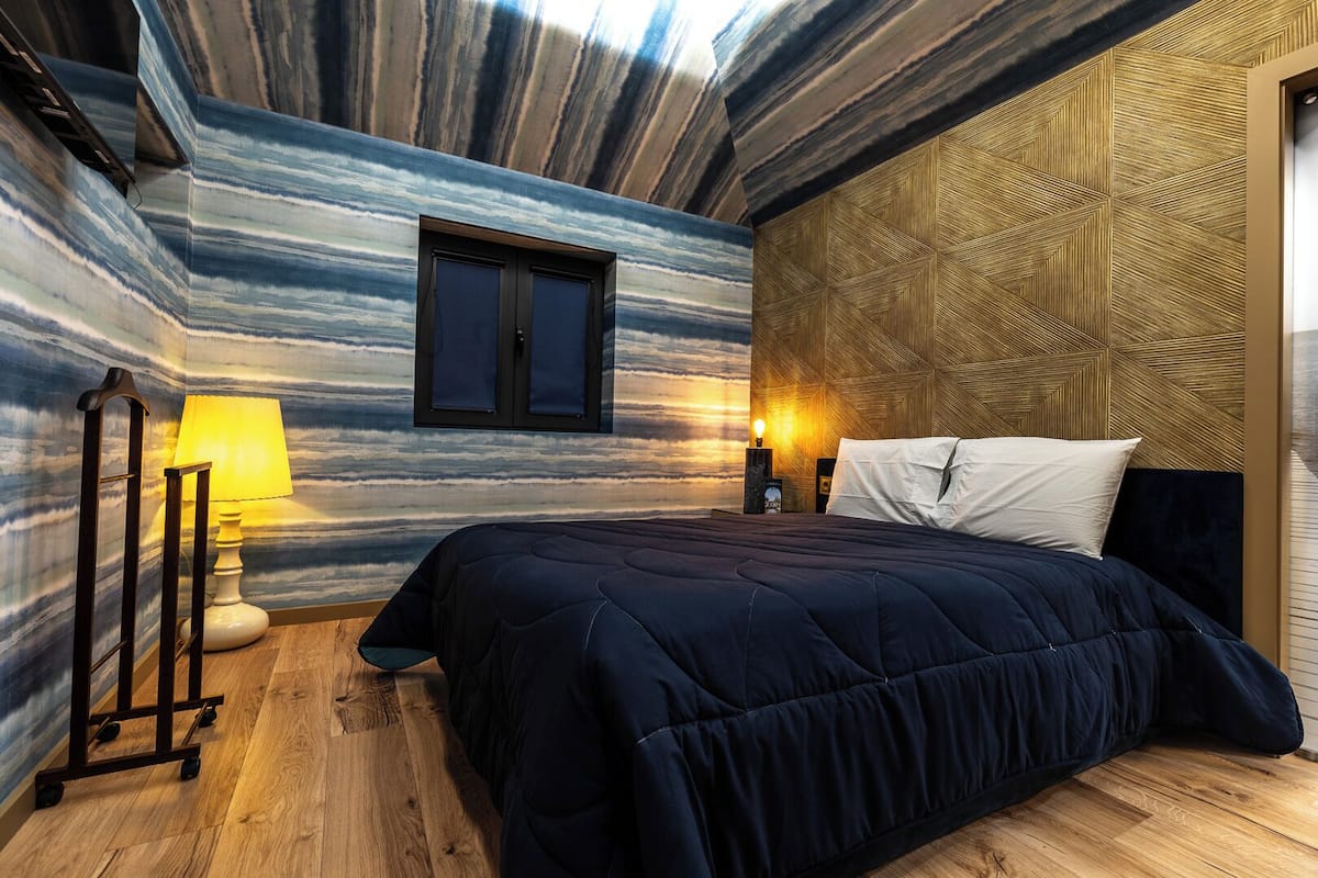 Un dormitorio con cama, mesita de noche, lámpara y ventana.