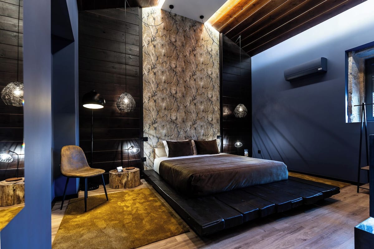 Un dormitorio moderno con cama, una silla, suelo de madera y un diseño de pared original.