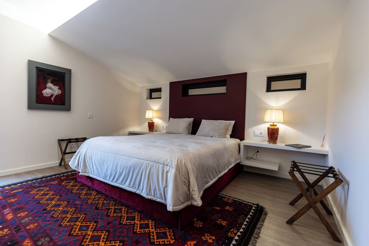 Un dormitorio con cama, lámparas de noche, una alfombra y un cuadro en la pared.